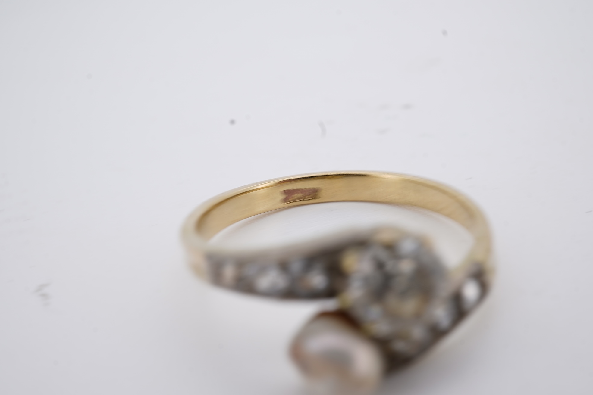 A yellow meta (stamped 18ct) cultured pearl and diamond set crossover ring, with six stone graduated diamond set shoulders, size M, gross weight 2.6 grams (pearl nacre a.f.).
